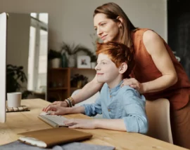 Woman leaning over child helping on PC