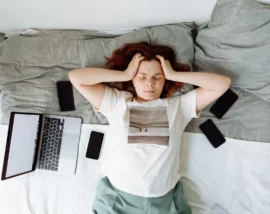 Woman surrounded by phones and laptop holding head